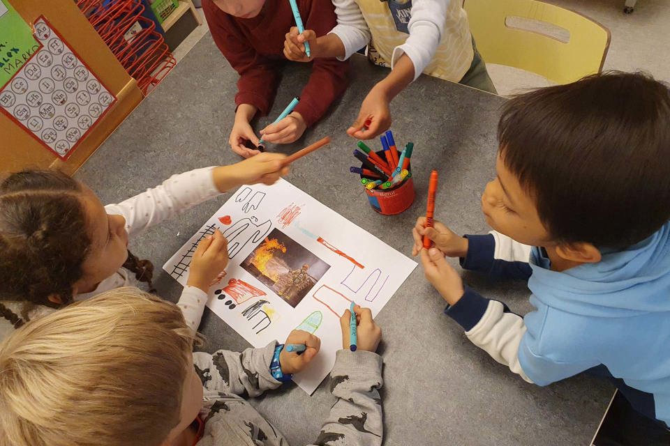 Children sitting around a table while drawing together on a paper.